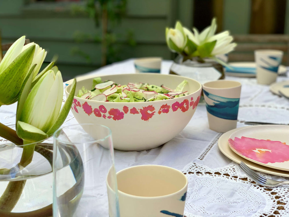 
                  
                    table setting with pink coral bamboo dinnerware layer for dinner on out door table with white tablecloth .
                  
                