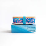 pink coral lunch box with turquoise strap on blue wave printed gift box.