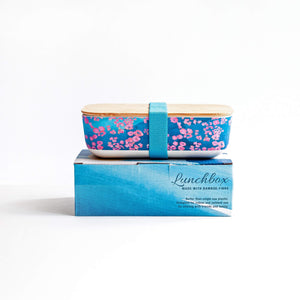 
                  
                    pink coral lunch box with turquoise strap on blue wave printed gift box.
                  
                