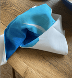 single organic fabric napkin with blue wave print on wooden table