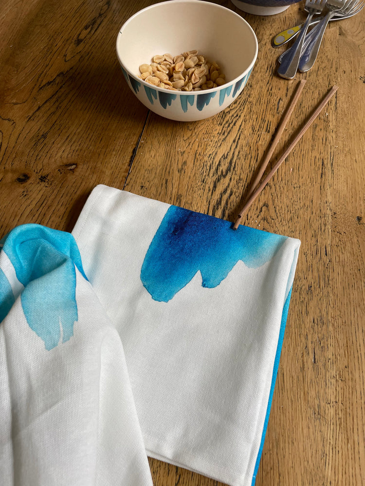 
                  
                     two cotton cloth napkins with blue wave print, with small bamboo bowl with blue wave containing peanuts with chop sticks and forks on wooden table
                  
                
